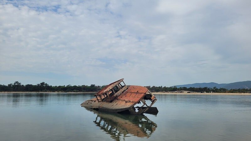 A rusted shipwreck partially submerged in calm coastal water best evokes an unidentified, mystery wreck with no clear origin.