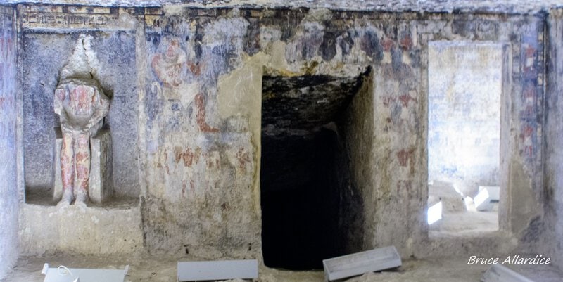 Shows the decorated interior of an ancient Egyptian rock-cut tomb at Saqqara with wall paintings and a burial chamber…