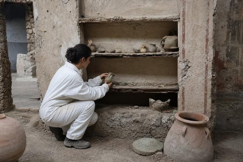 A researcher examines artifacts at a Pompeii excavation site like those yielding sealed cupboards still containing coins,&hellip;