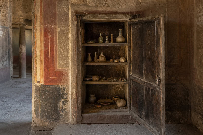 A Pompeii cupboard of the kind sealed since AD 79, its shelves preserving coins, amulets